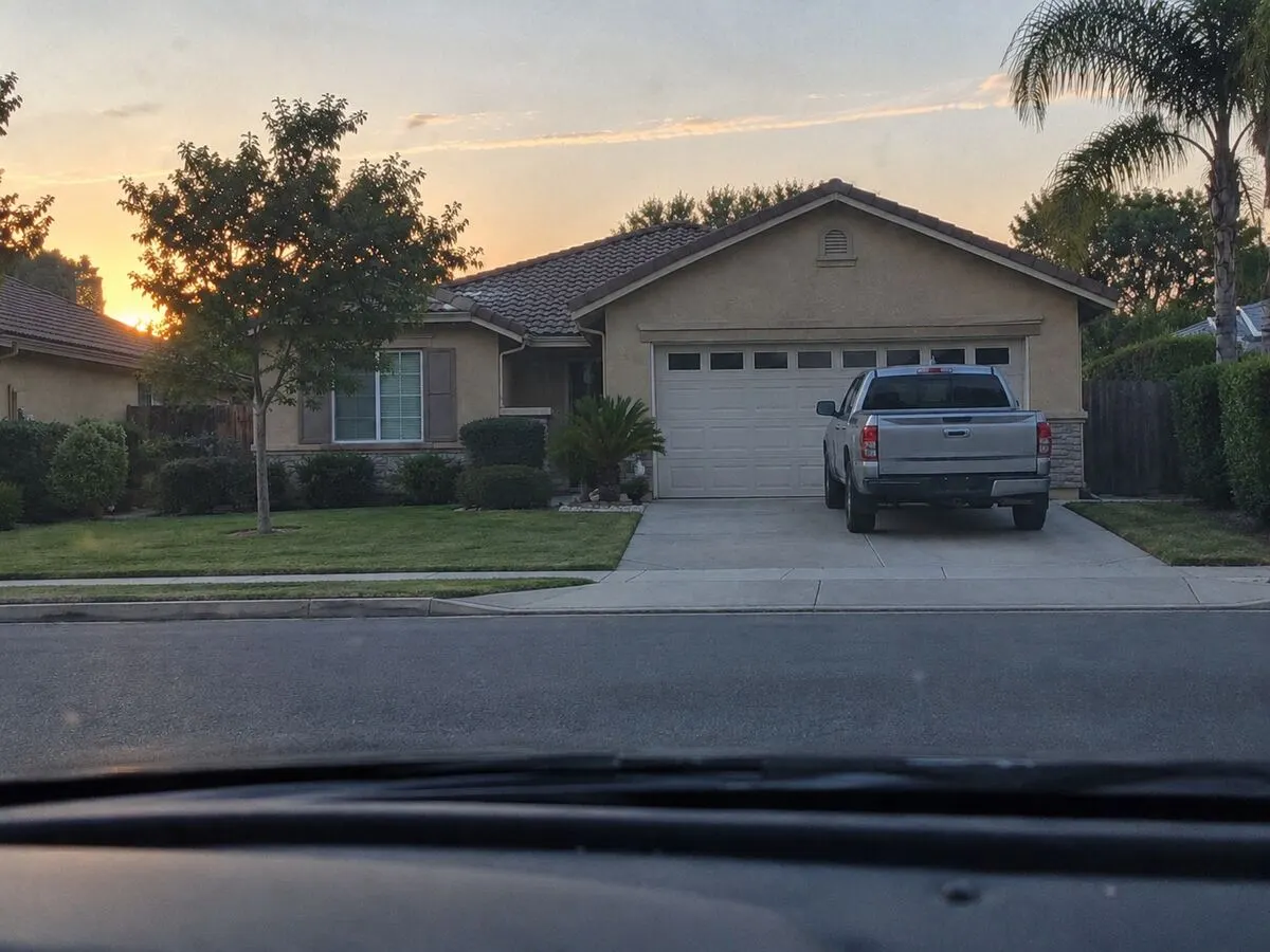 Dawn view through a car windscreen of a quiet street with a pickup parked on a driveway