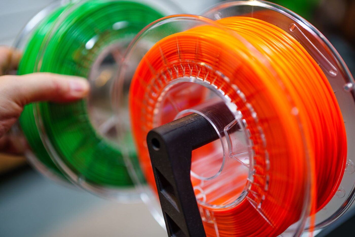 Spools of orange and green 3D printer filament being handled