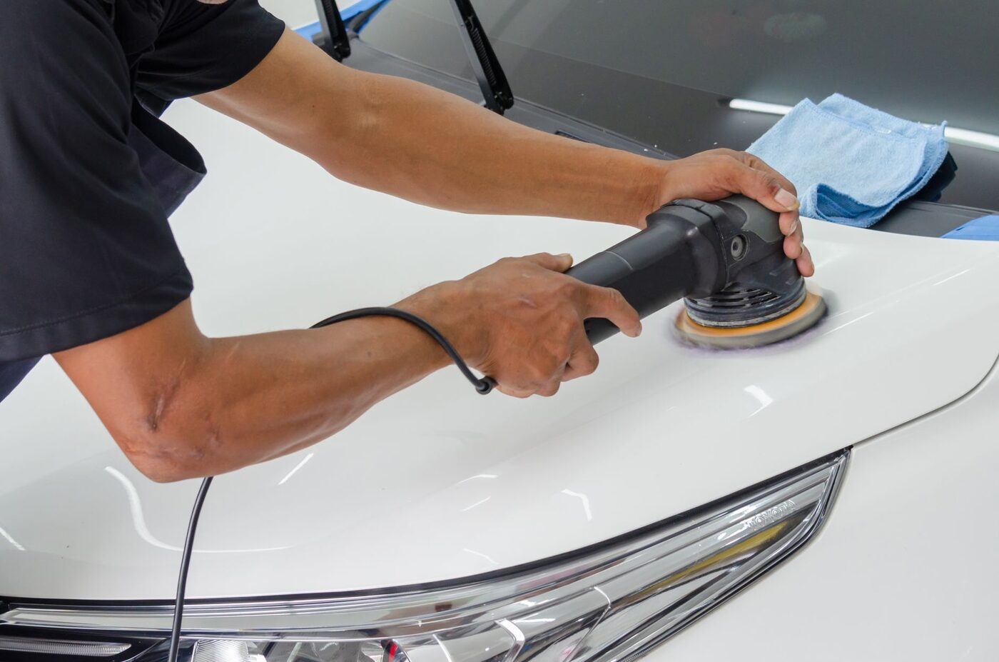 A rotary polisher being worked across a white car bonnet