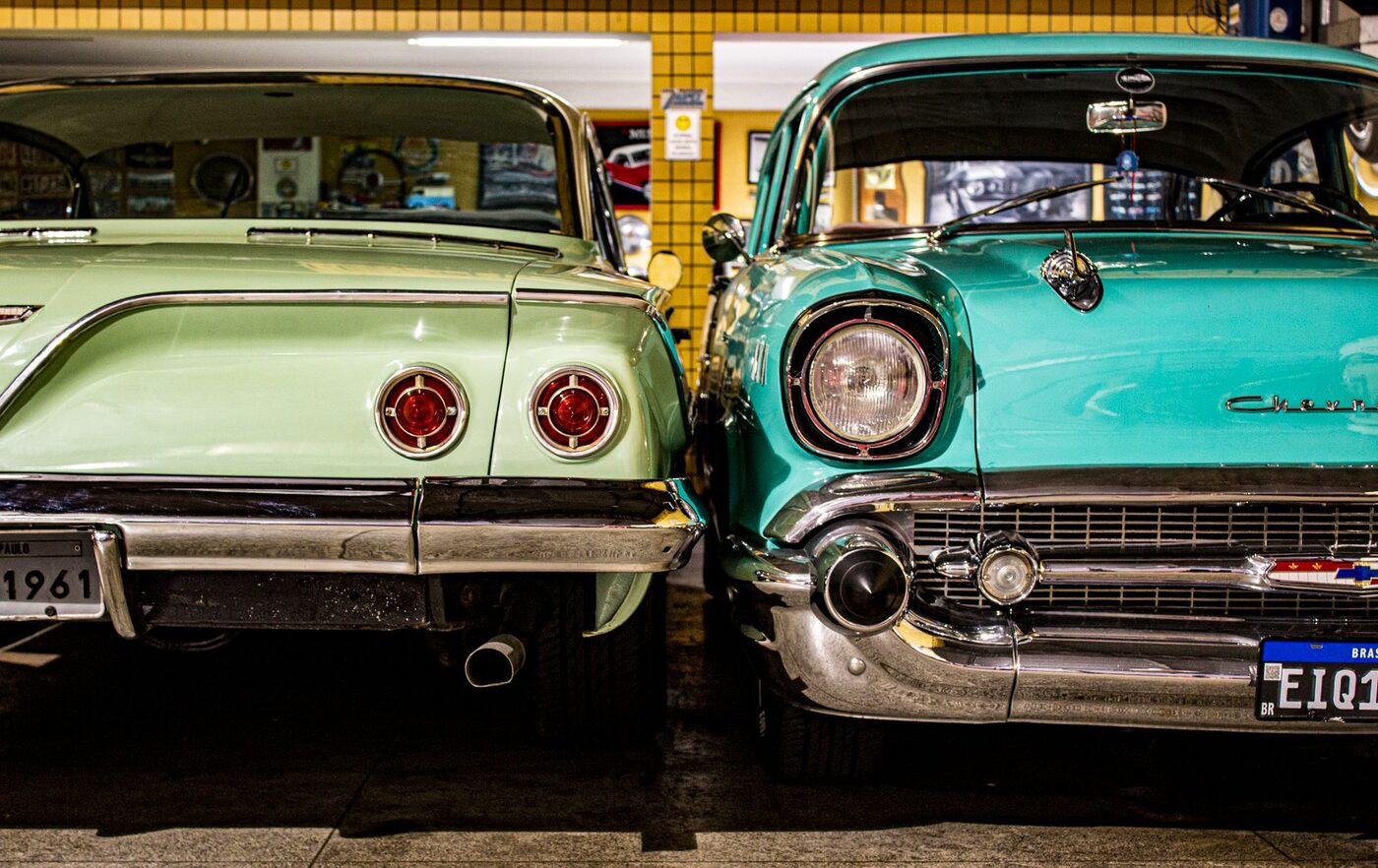 Two restored 1950s American cars parked nose to nose in a garage