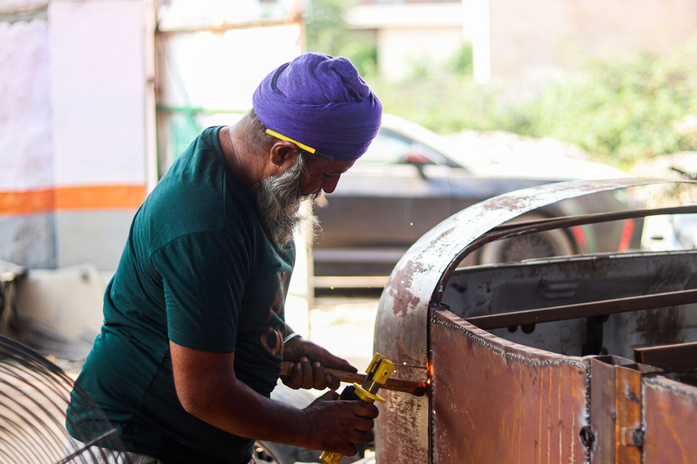 Someone working with hand tools on the bare rusted panel of an old car