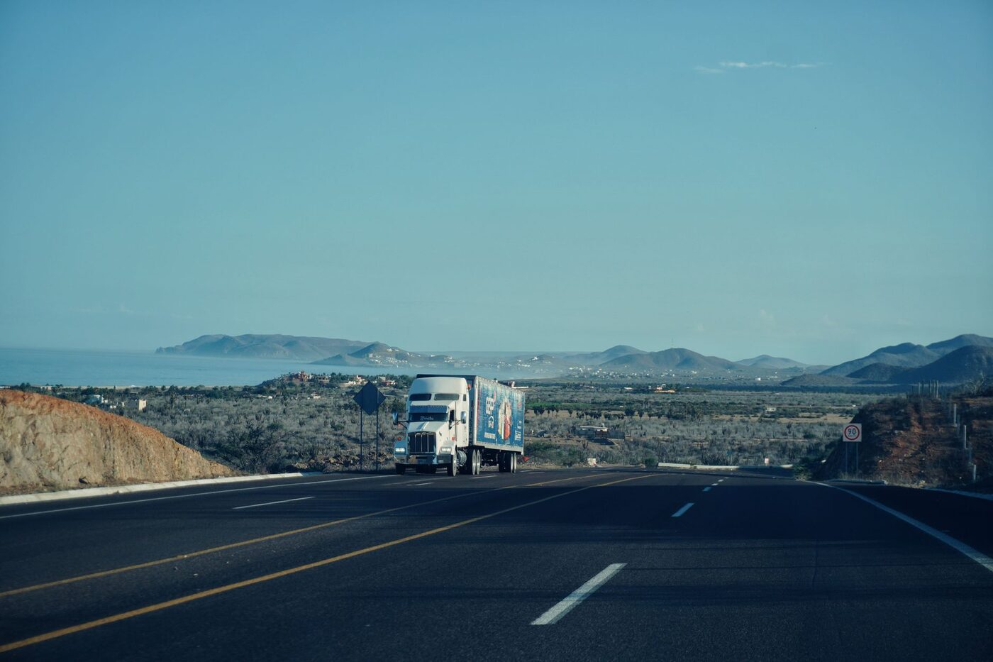 A semi truck travelling on a highway with mountains behind it