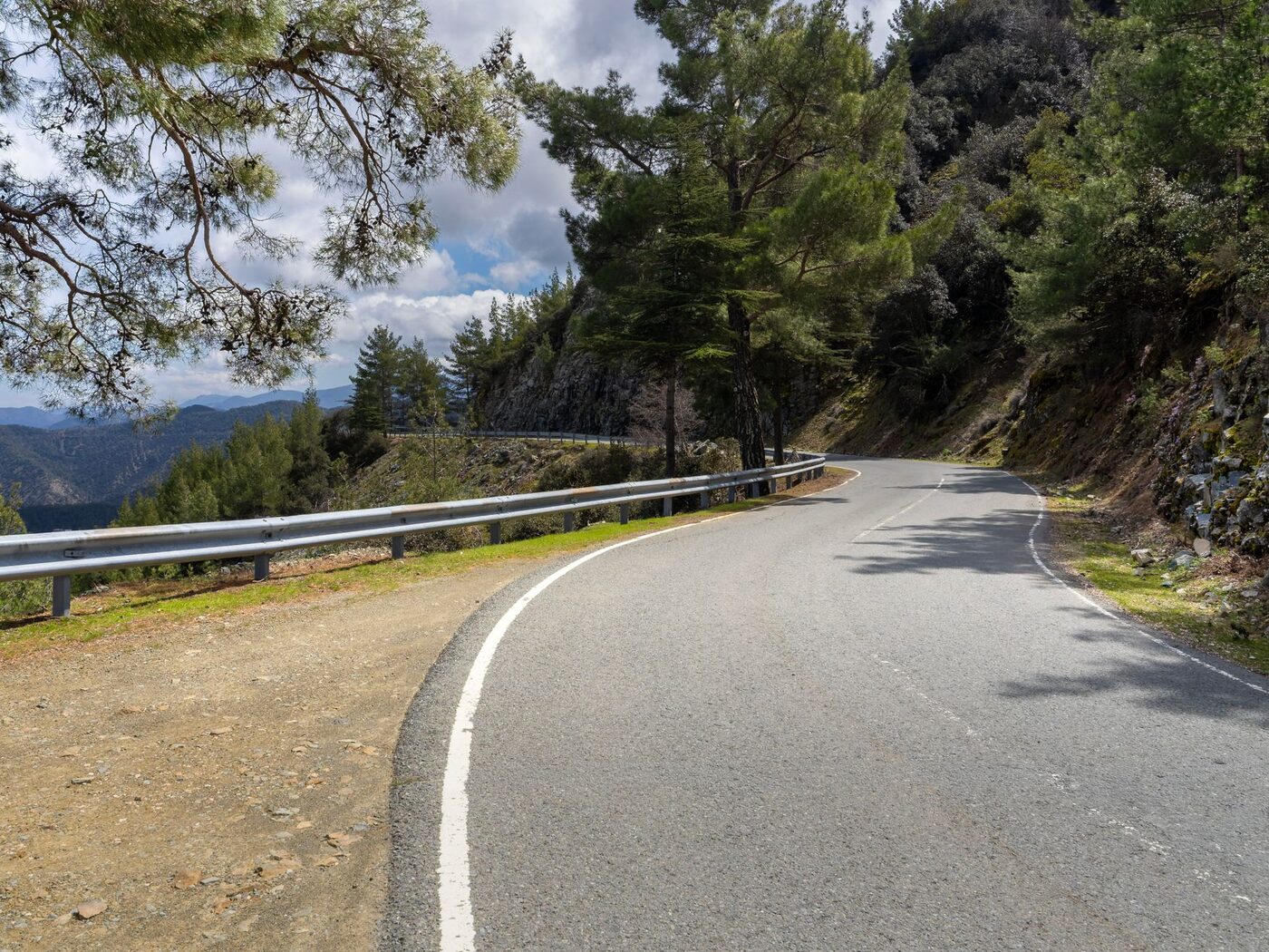 A mountain road with a metal guardrail curving along the edge
