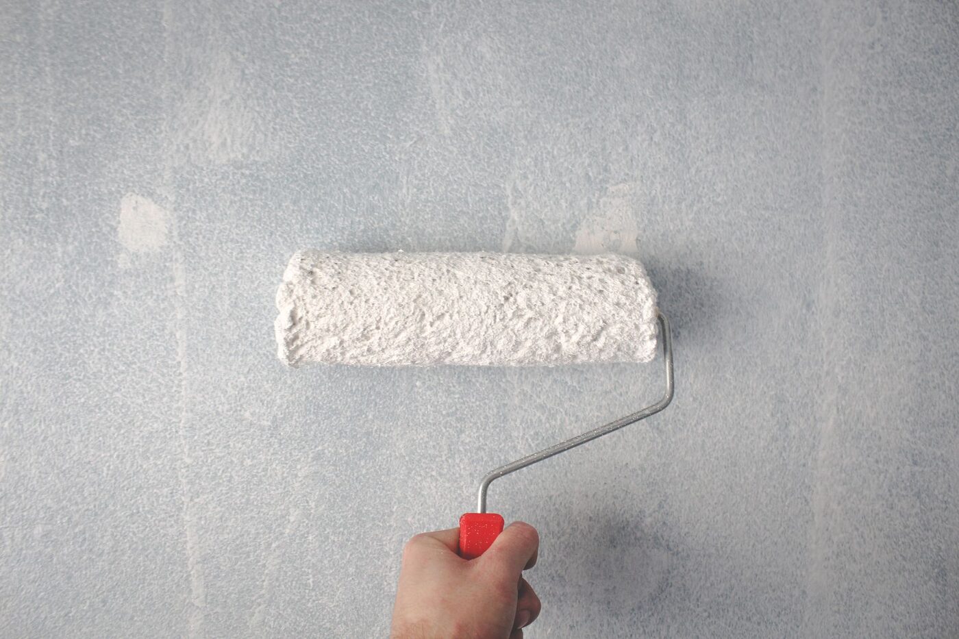 A hand rolling white paint onto an interior wall