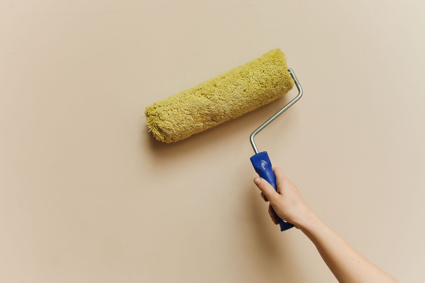 A hand rolling paint onto a beige wall with a roller