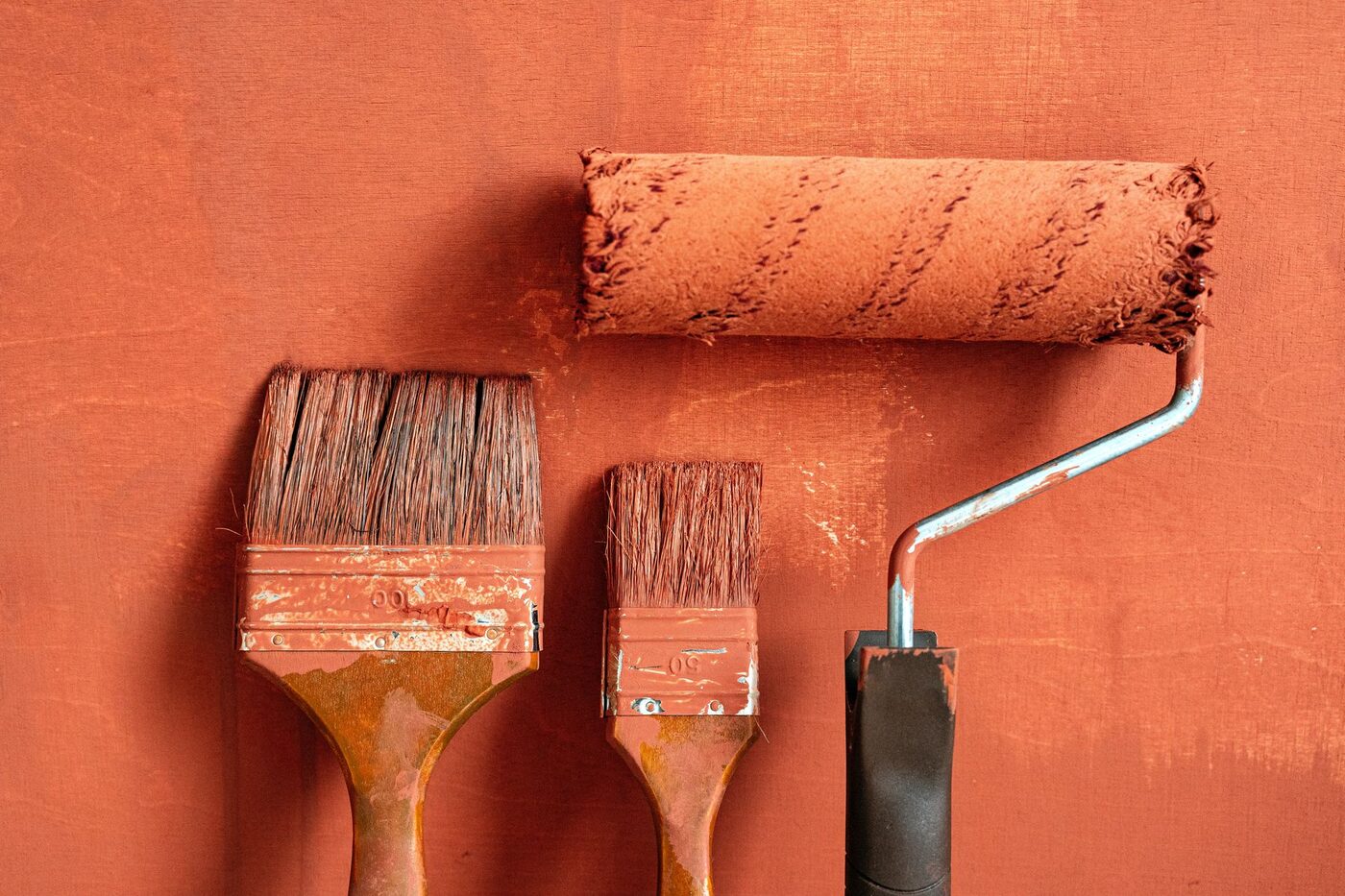 Paint brushes and a roller laid on an orange painted surface