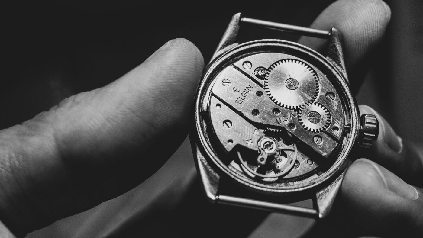 A mechanical watch movement held in the hand with the gear train visible