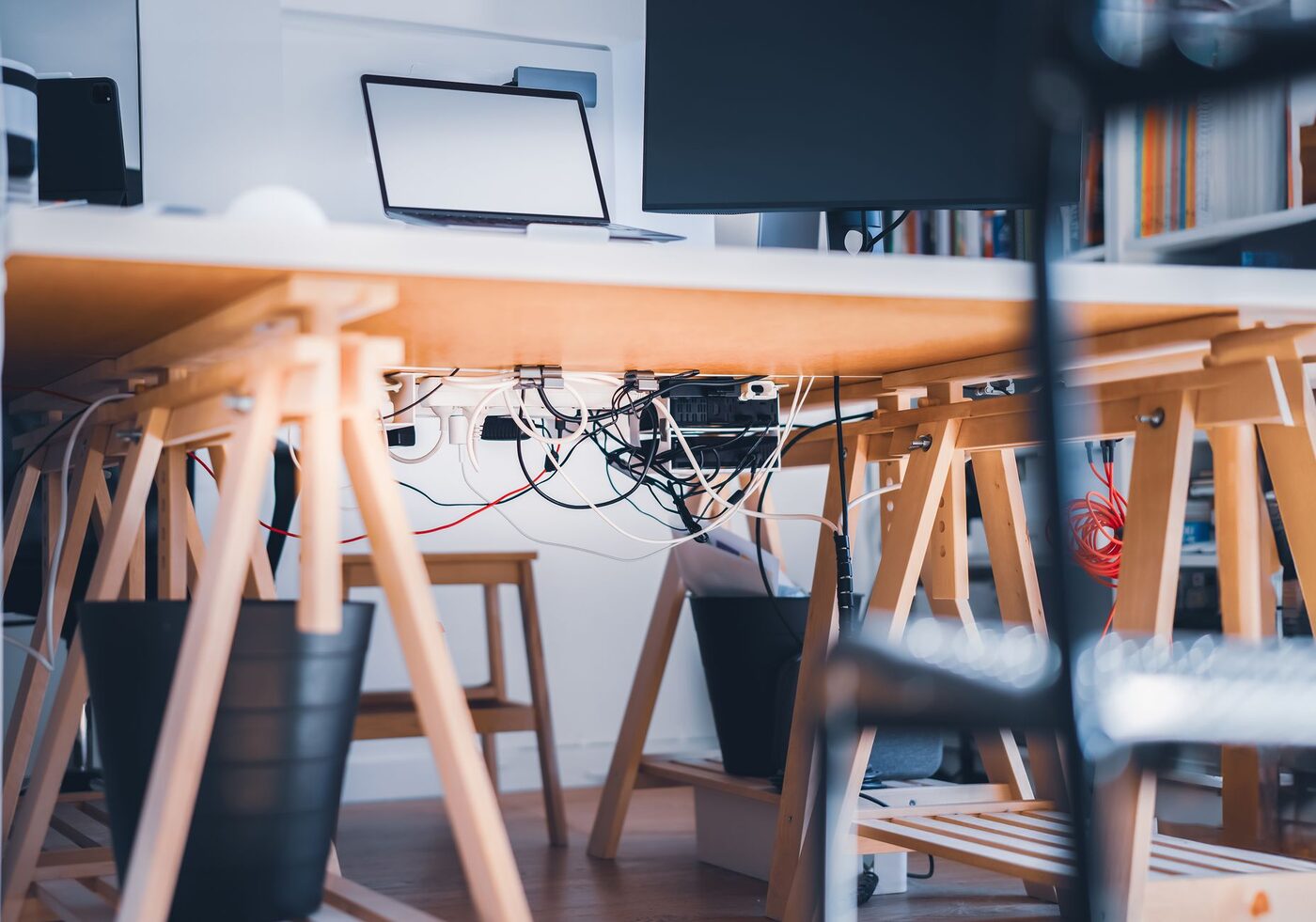 A tangle of power cables, plugs and adaptors under an office desk beside a laptop and monitor