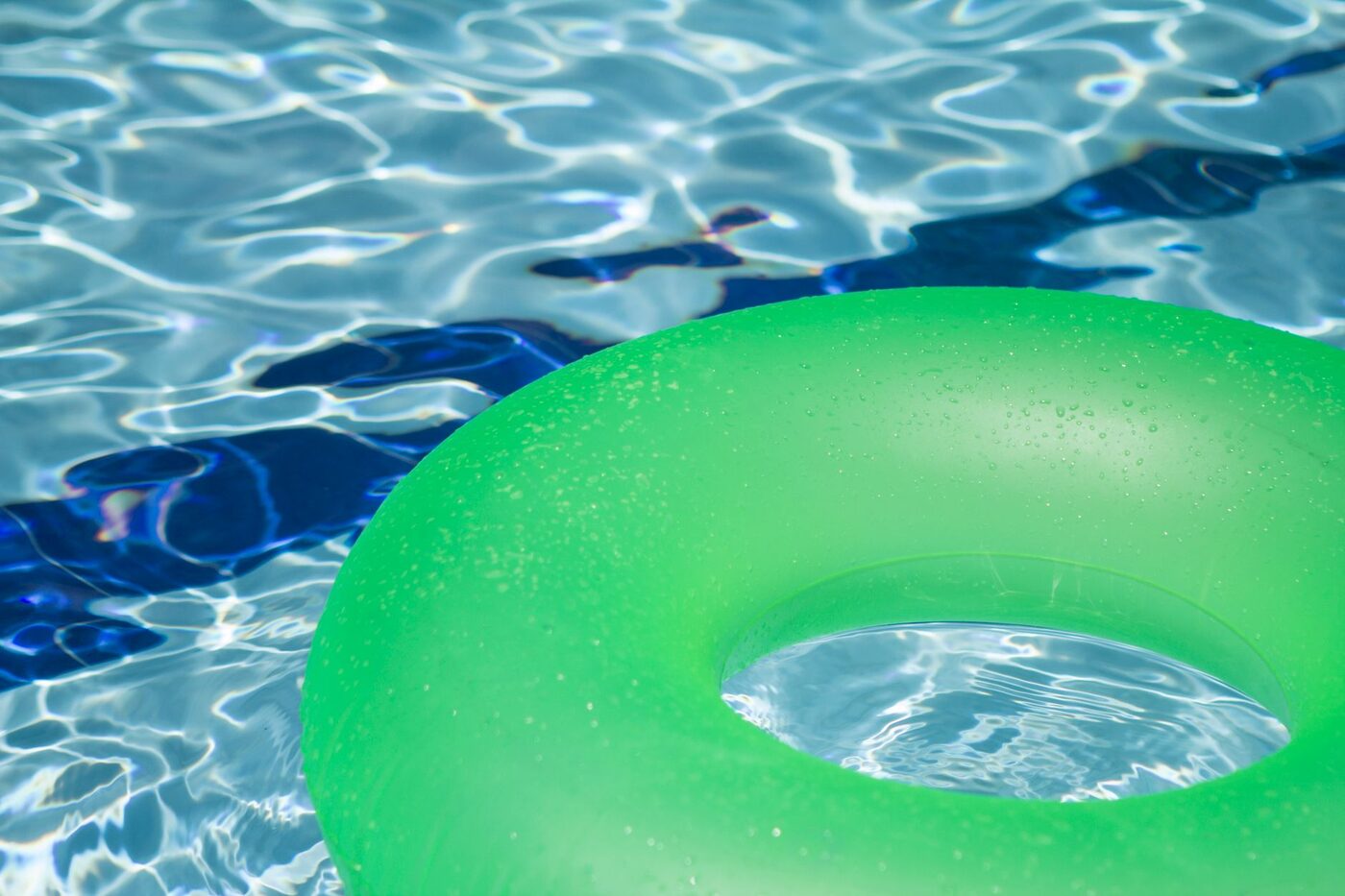 A green inflatable ring floating on the surface of a clear blue swimming pool