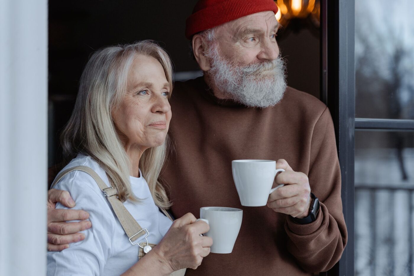 A retired couple sitting together with mugs of coffee, looking out of a window