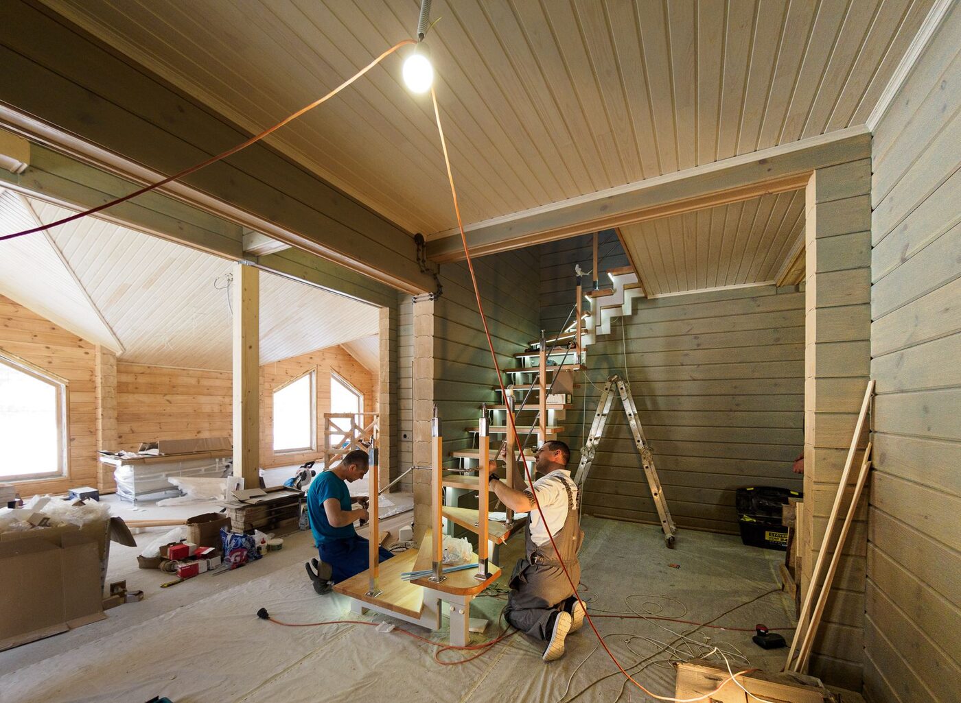 Two carpenters assembling a wooden staircase inside a timber-lined interior
